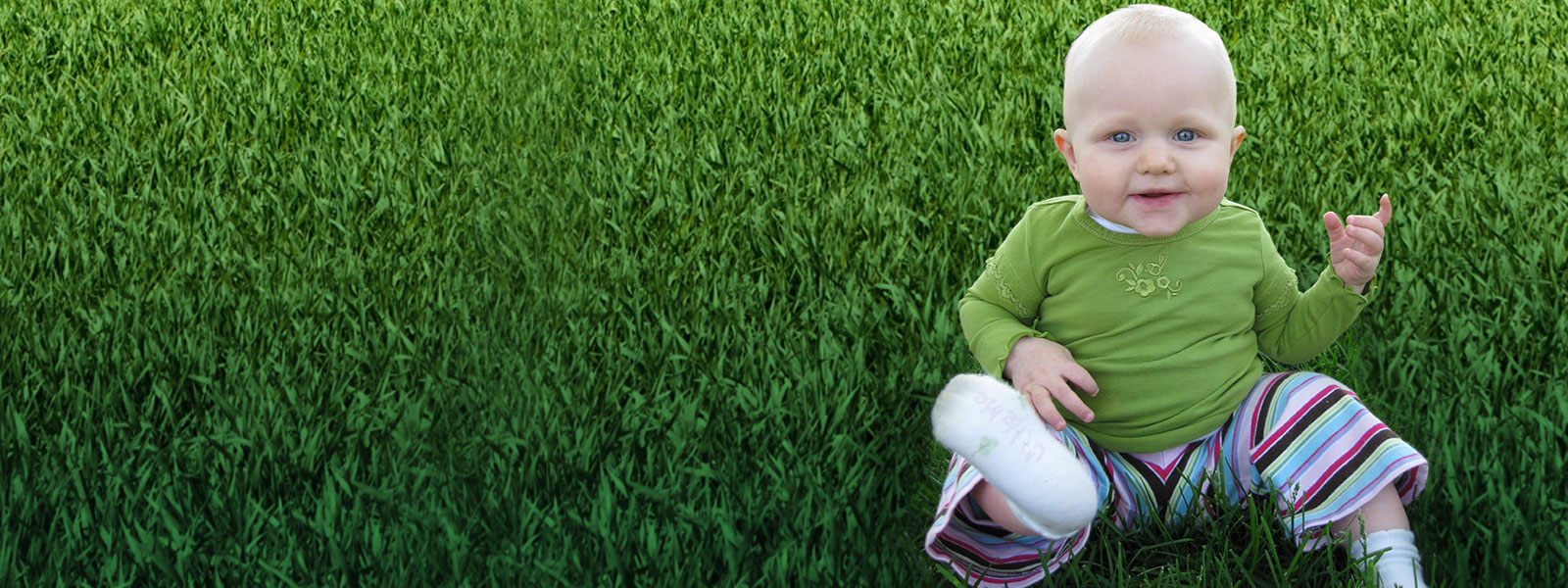 A baby sitting in a field of green grass